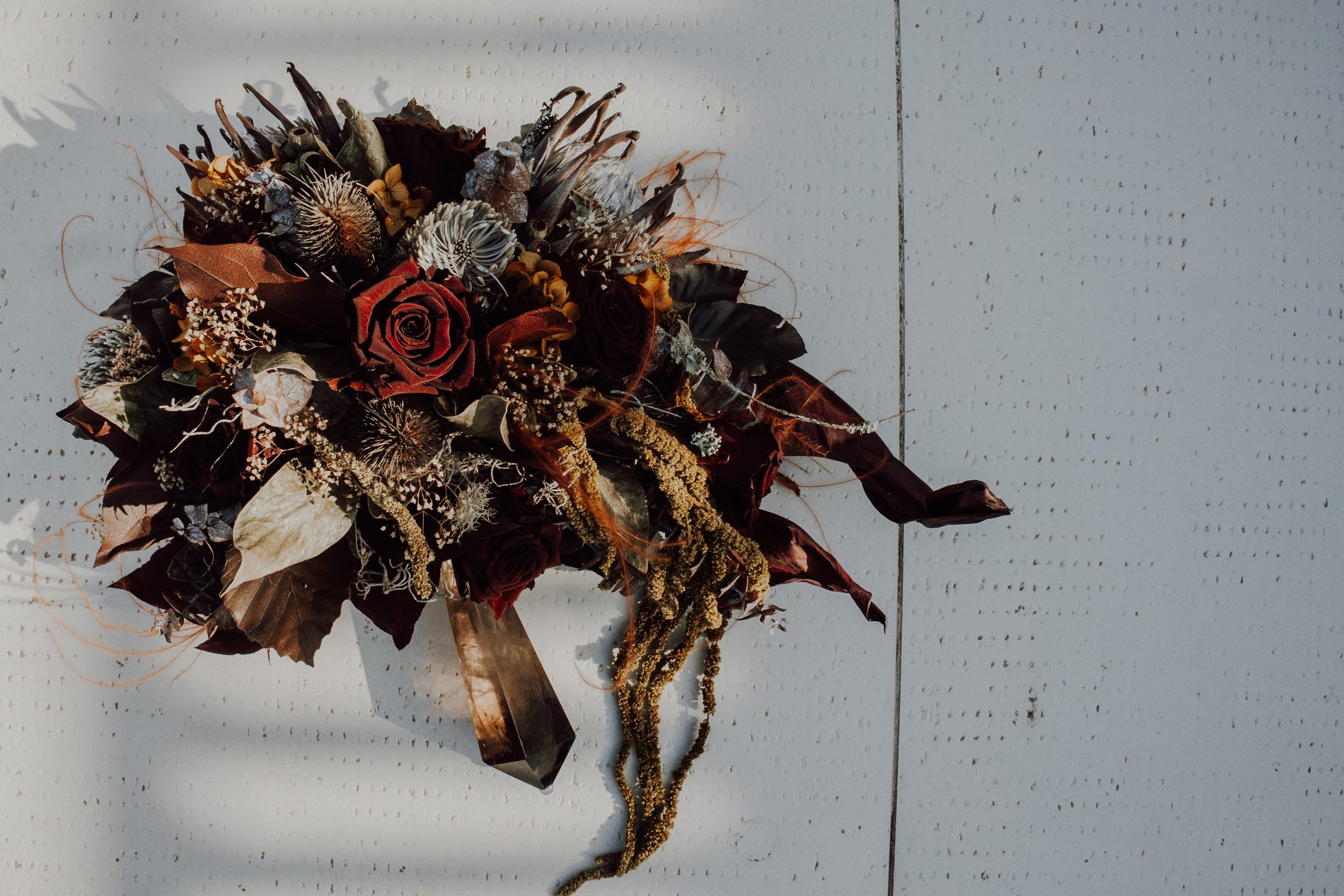 A moody dried bouquet of burgundy roses, protea and quartz