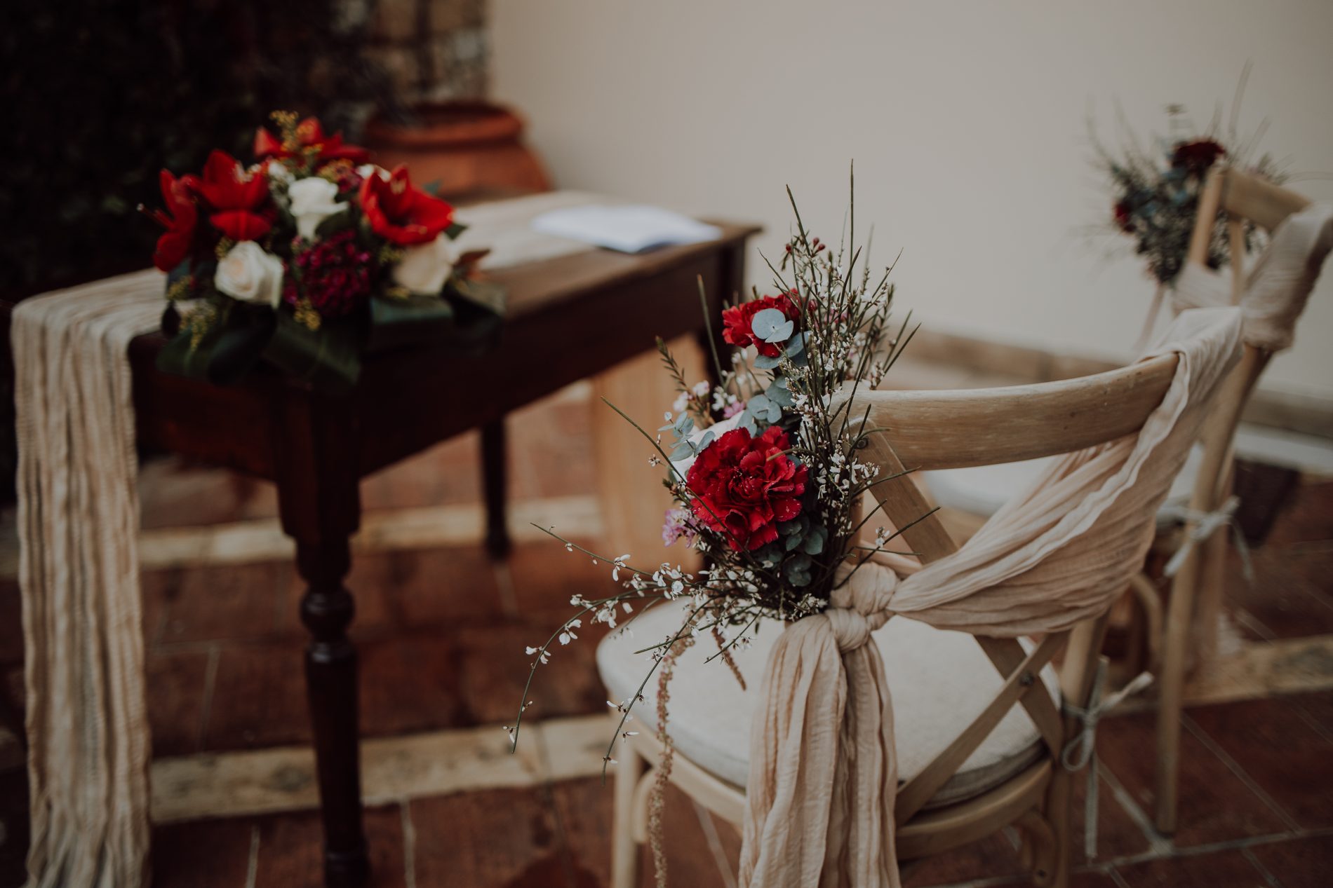 Ceremony florals in deep reds on the signing table and chairs