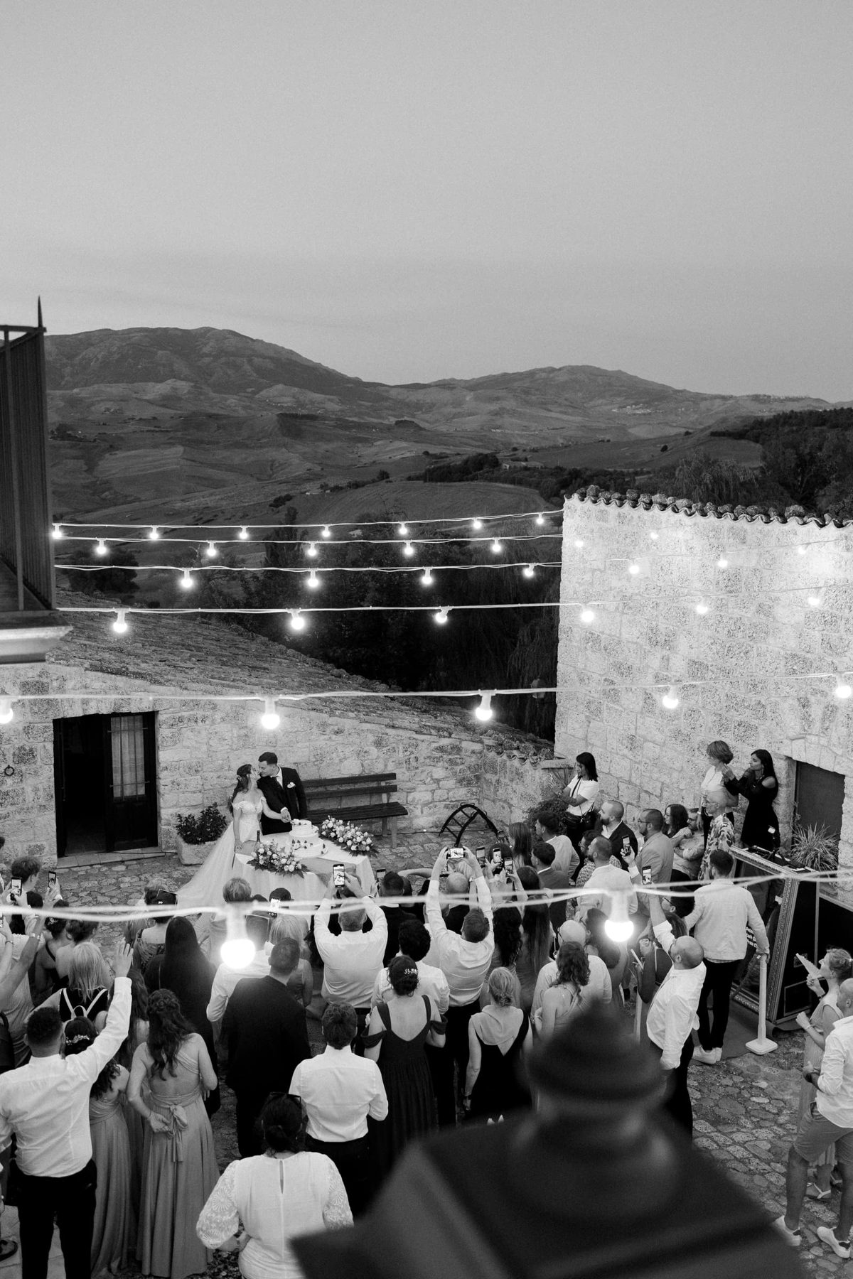 Guests gathered under string lights for the cake cutting