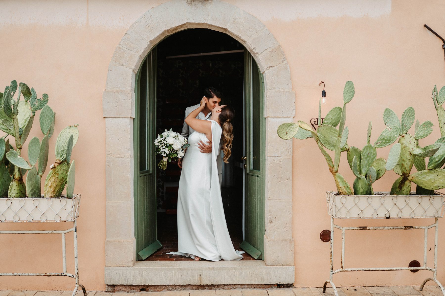 A kiss in the green arched doorway framed by prickly pears