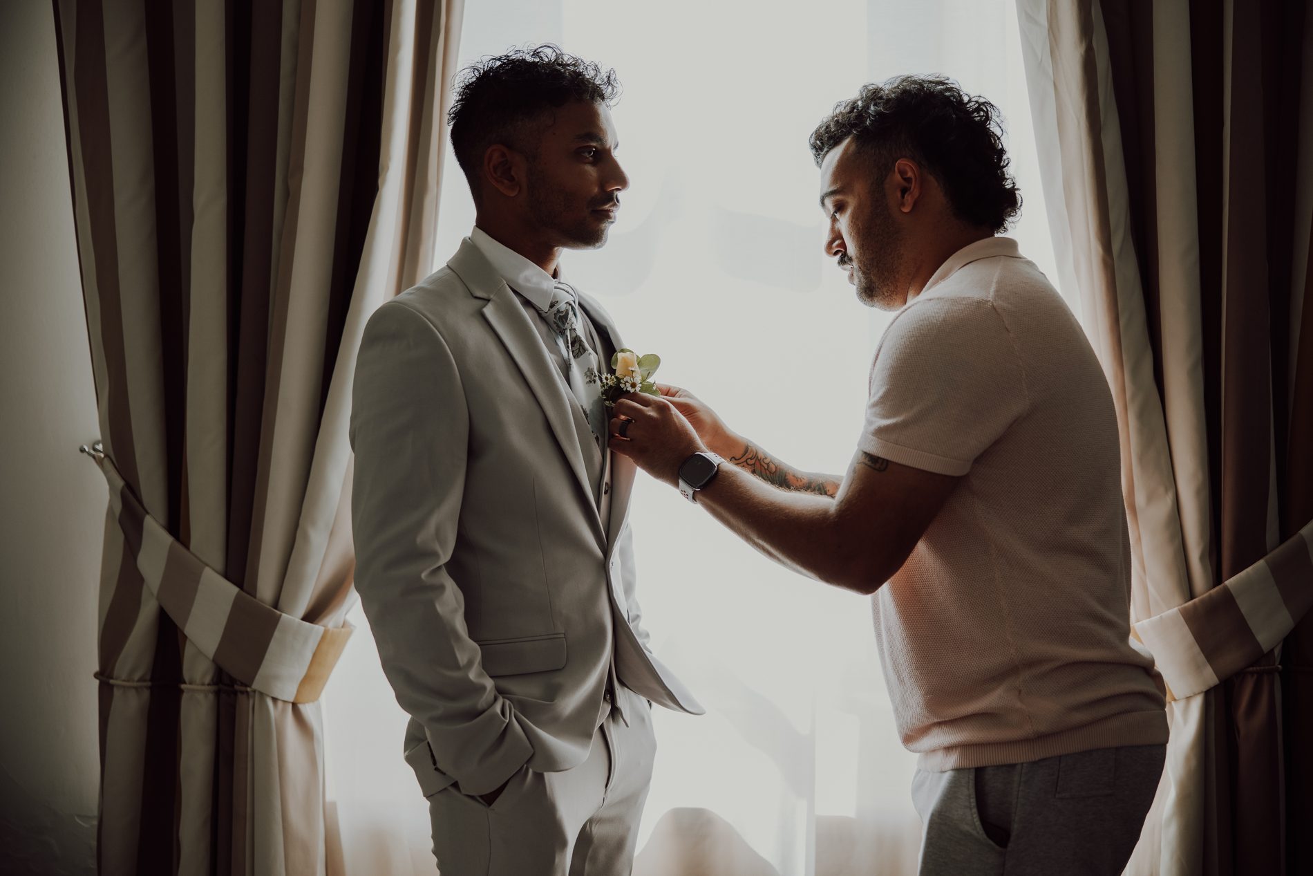 The groom getting ready, a boutonnière pinned in window light