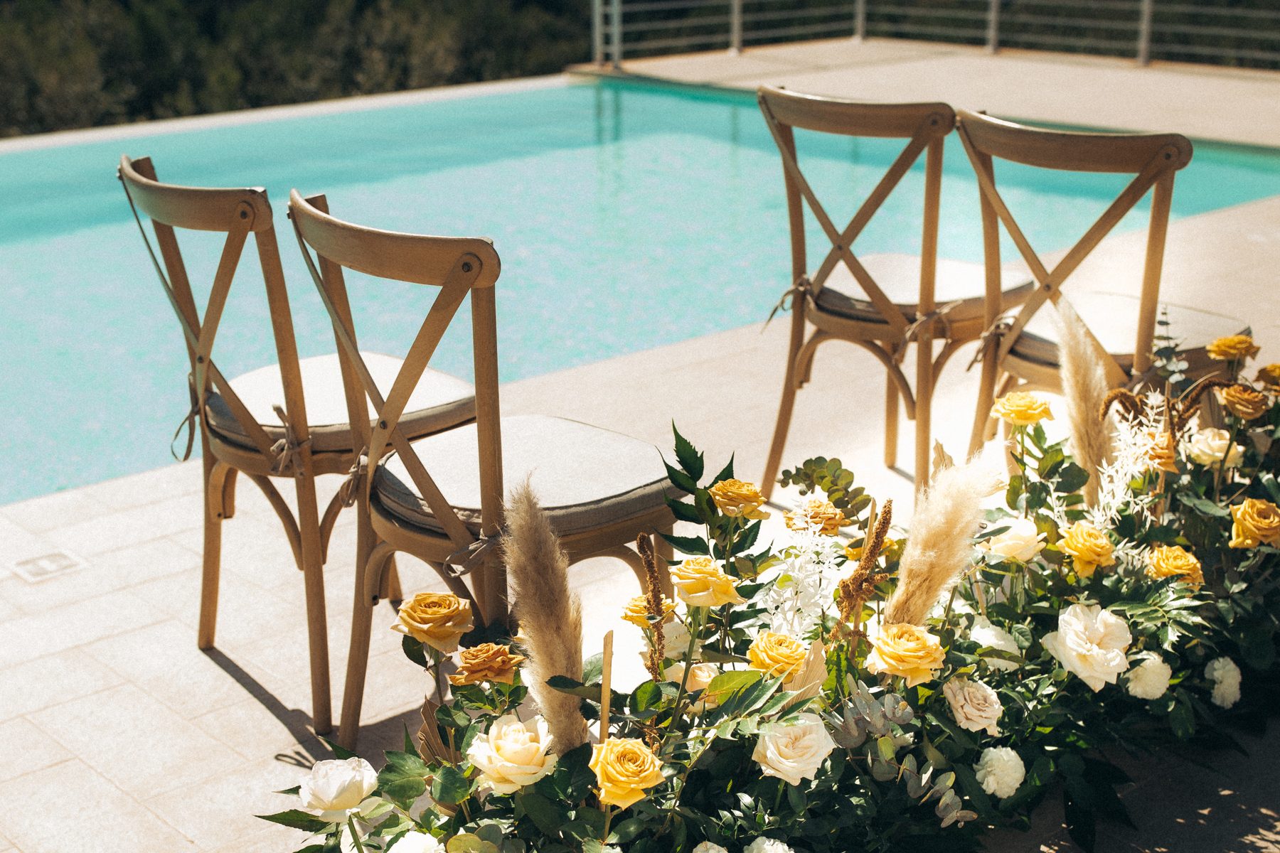 Cross-back chairs and soft roses and pampas beside the pool
