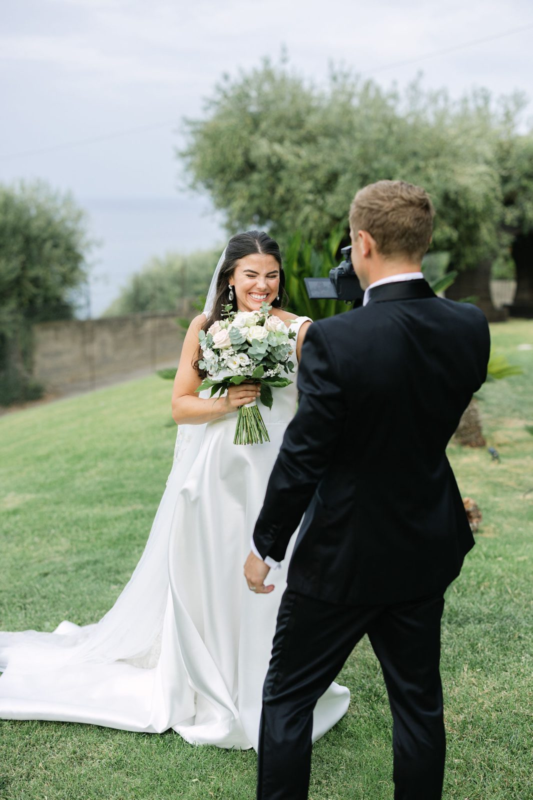 The first look — the bride, laughing, bouquet in hand