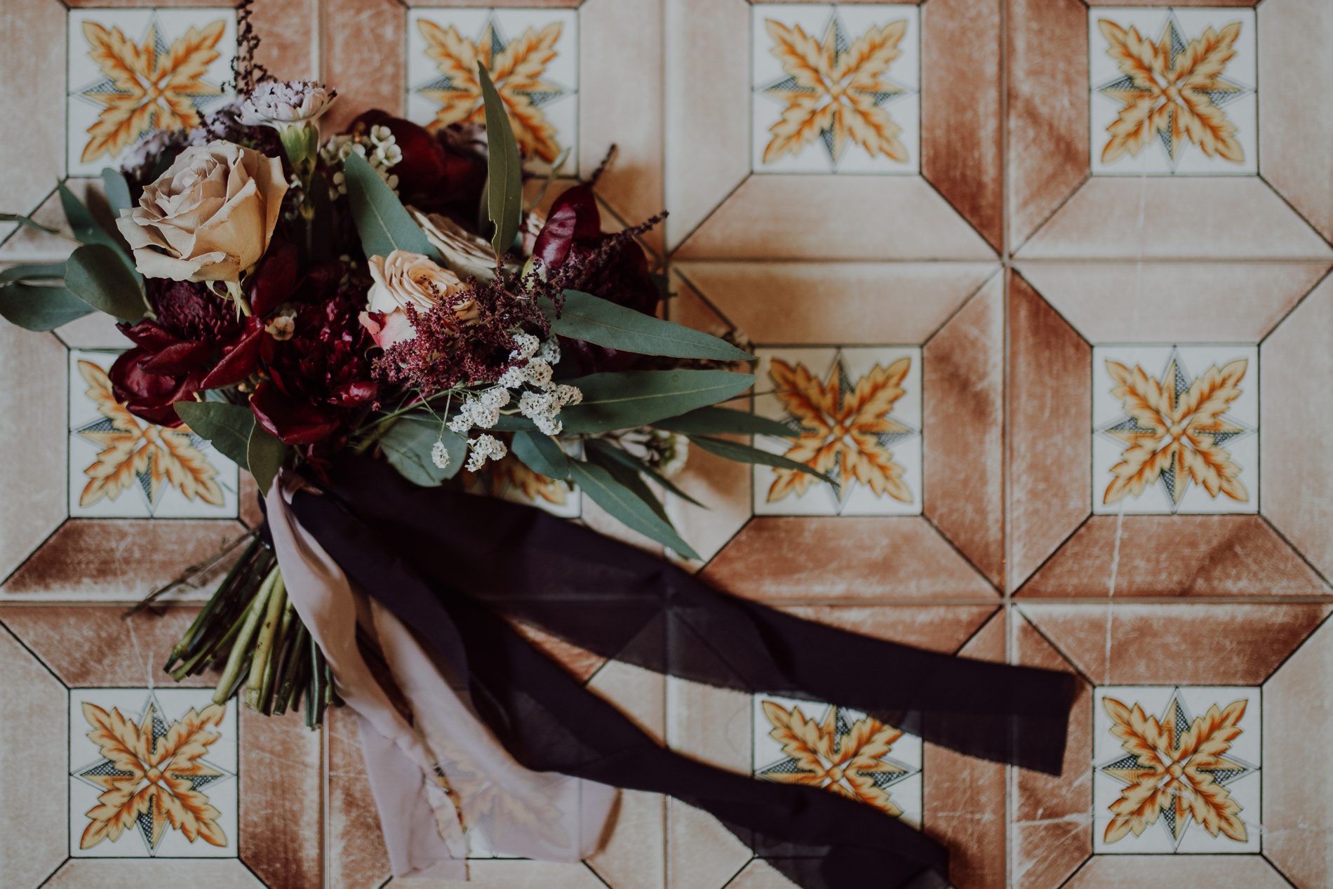 The bouquet — burgundy, blush and deep greens — on old Sicilian tile
