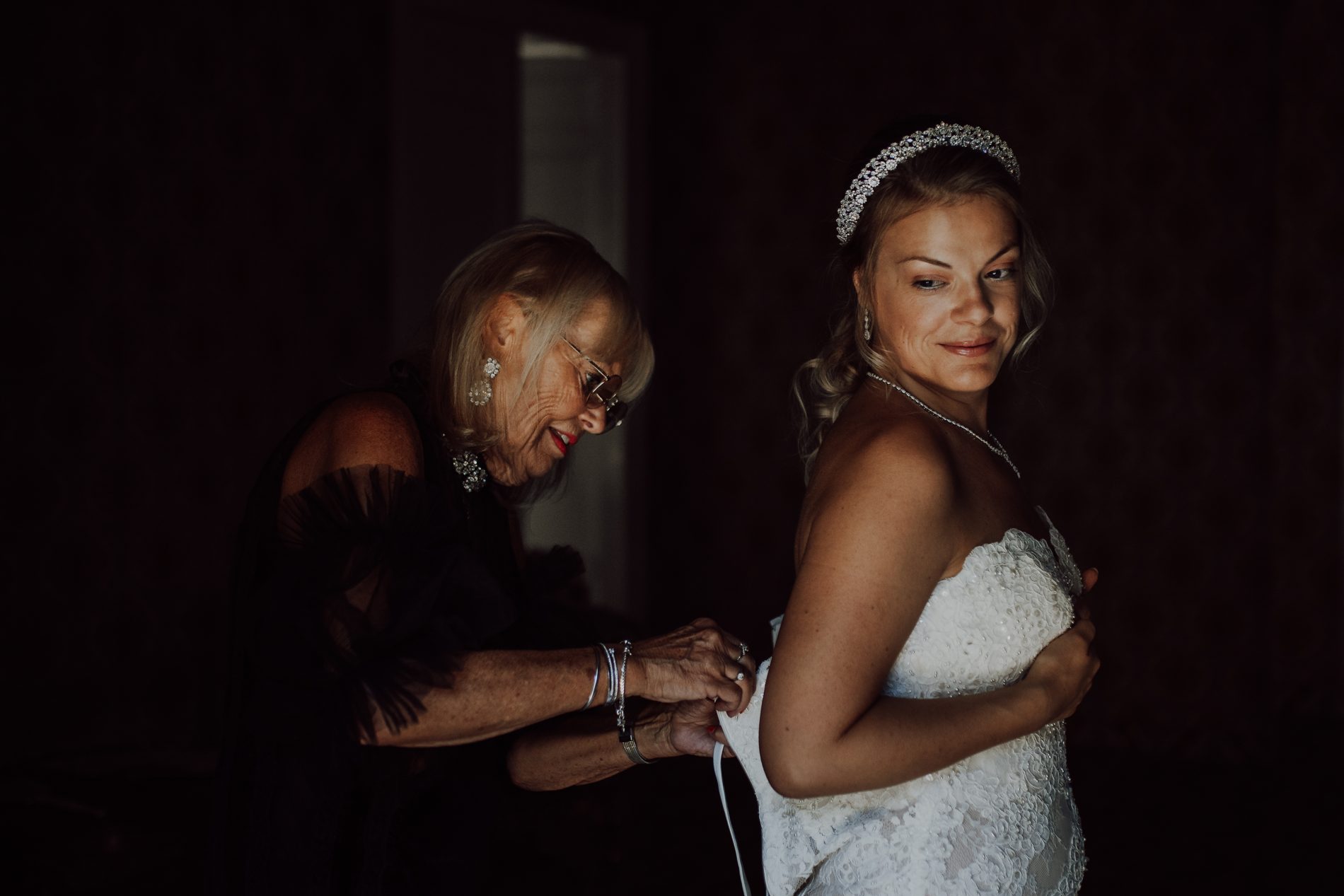 The bride laced into her gown in low, painterly light