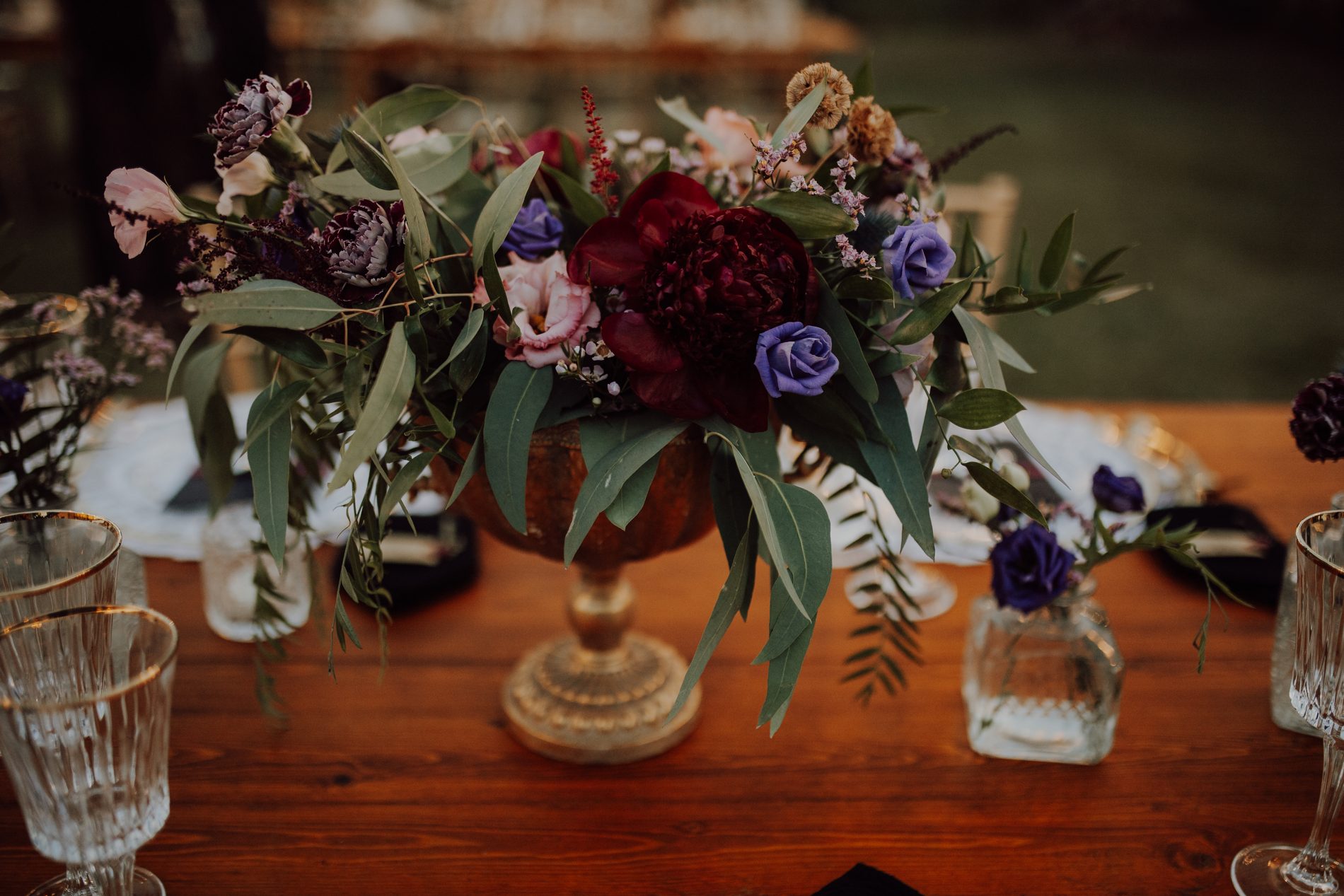 A gold chalice overflowing with burgundy and purple blooms